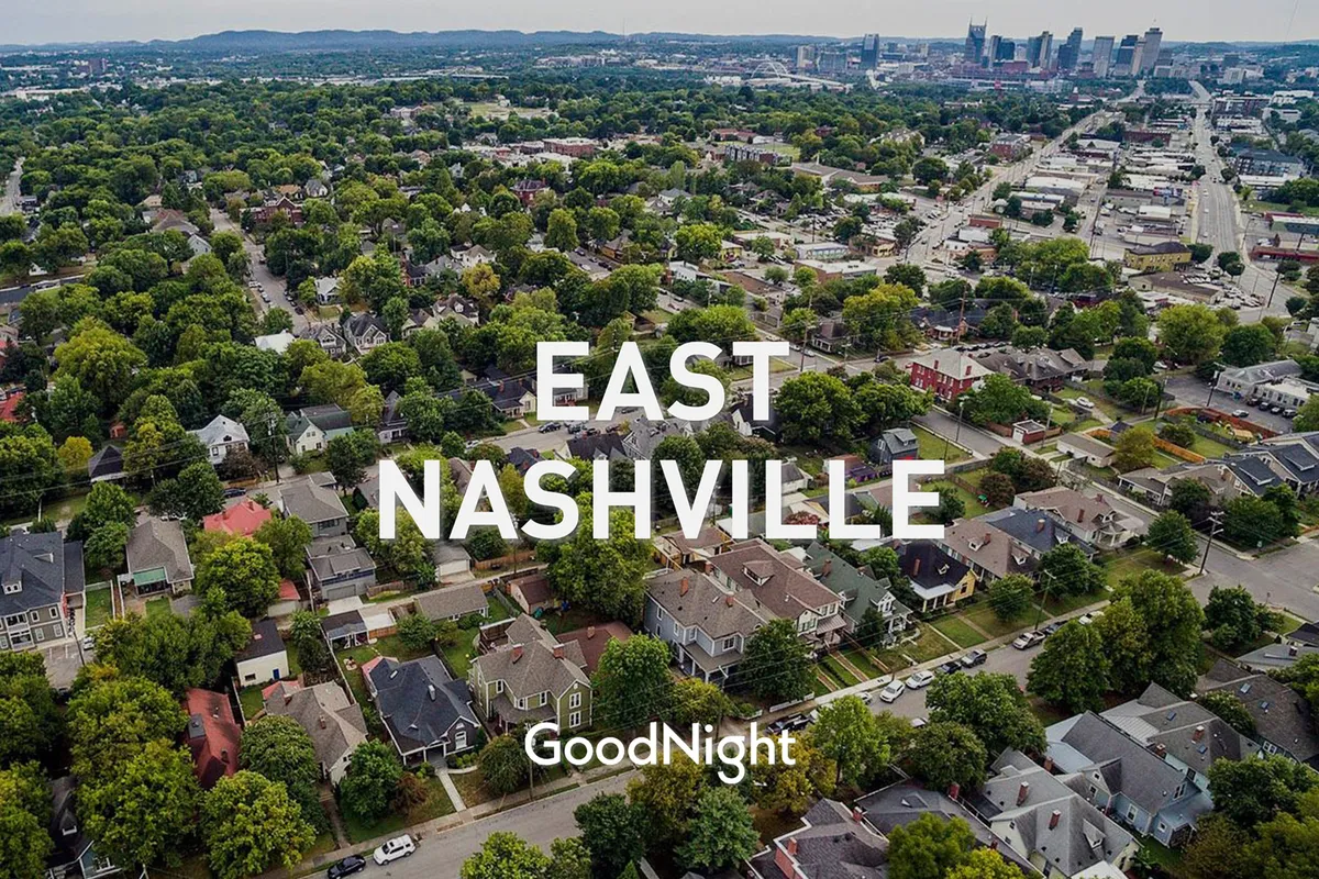 A picturesque neighborhood view featuring residential homes, lush greenery, and Nashville's urban skyline in the background. The image evokes the experience of strolling the area, visiting parks, or exploring local cafes.