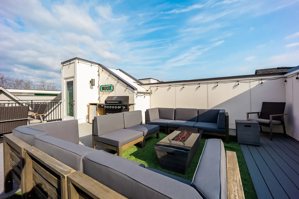 The hero image showcases an inviting outdoor rooftop deck with a cozy seating area, a grill ready for barbecues, and a stylish fire pit. The space is designed for relaxation and social gatherings, perfect for enjoying sunset views or starlit evenings with friends and family.