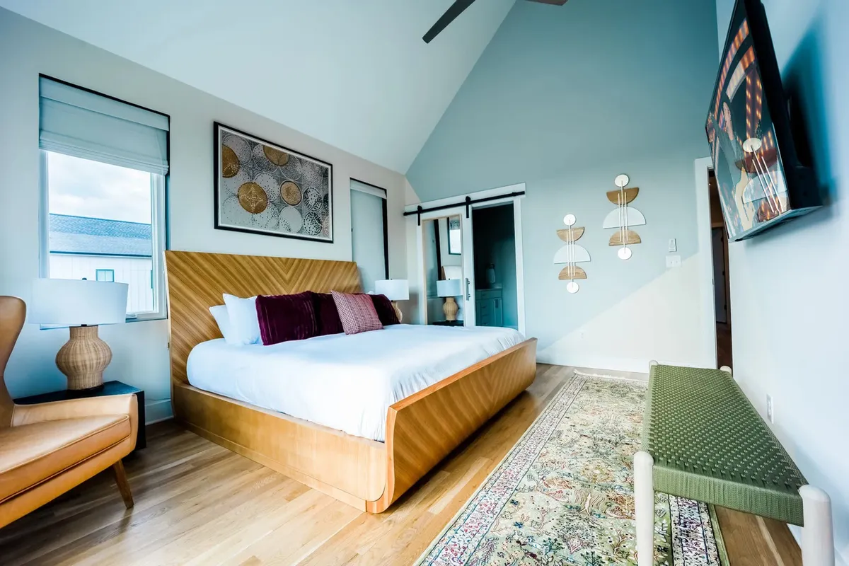 A tranquil and modern bedroom with a comfortable bed, stylish wall art, an accent armchair, and decorative wall lights. The room invites relaxation, with a hint of personal sanctuary, perfect for quiet mornings or evenings.