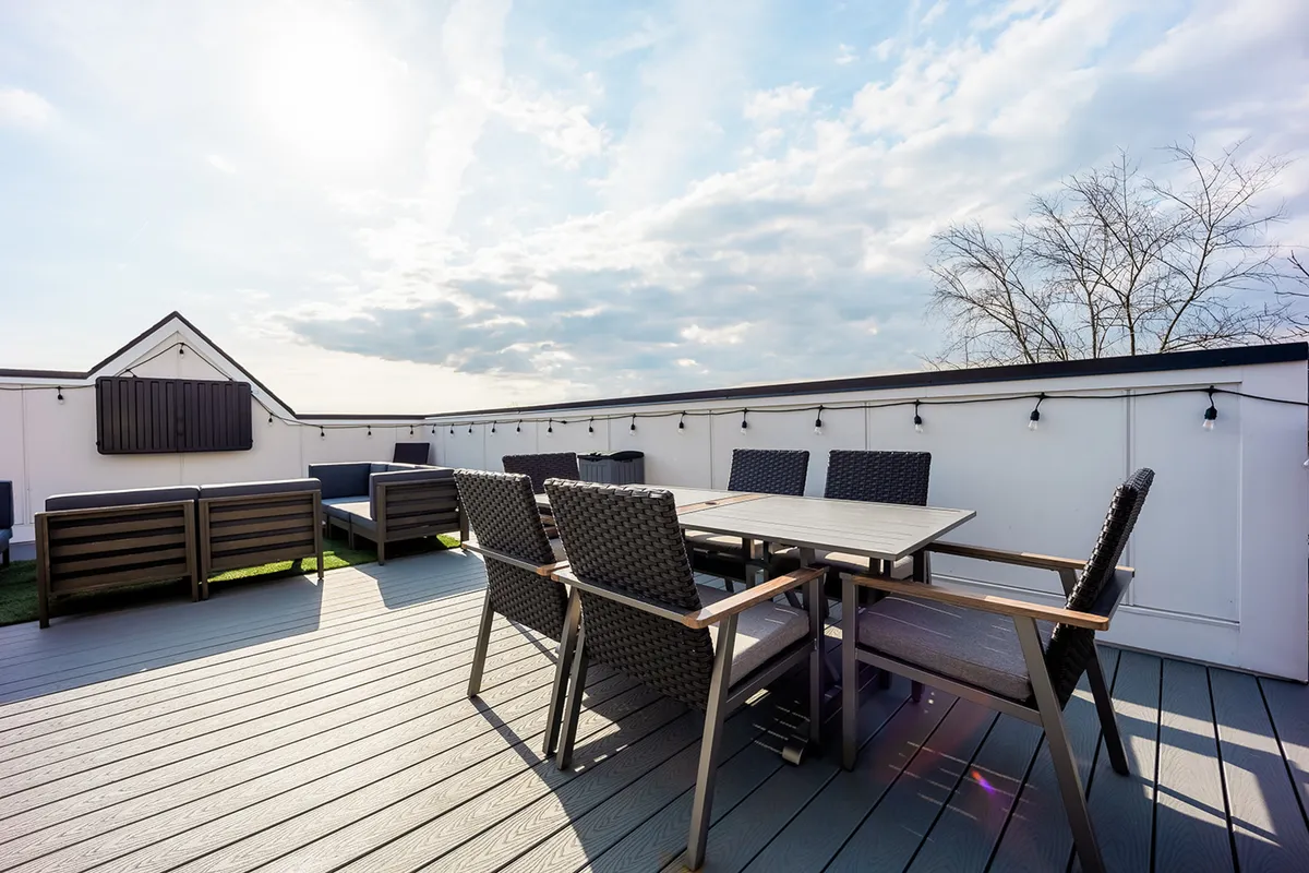 A chic rooftop space featuring a large outdoor dining table, lounge seating, and decorative string lights overhead. The city skyline shimmers in the distance, setting the stage for sunset dinners and evening celebrations.